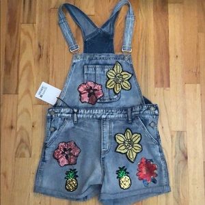 Lightly washed short overalls with floral patches.
